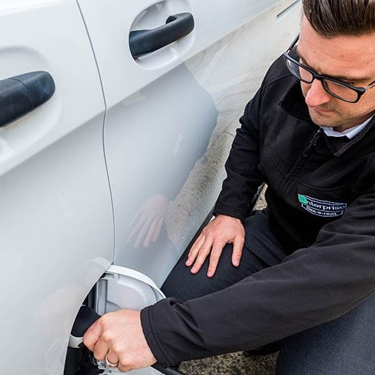  A man in a black casual jacket charging a white electric vehicle