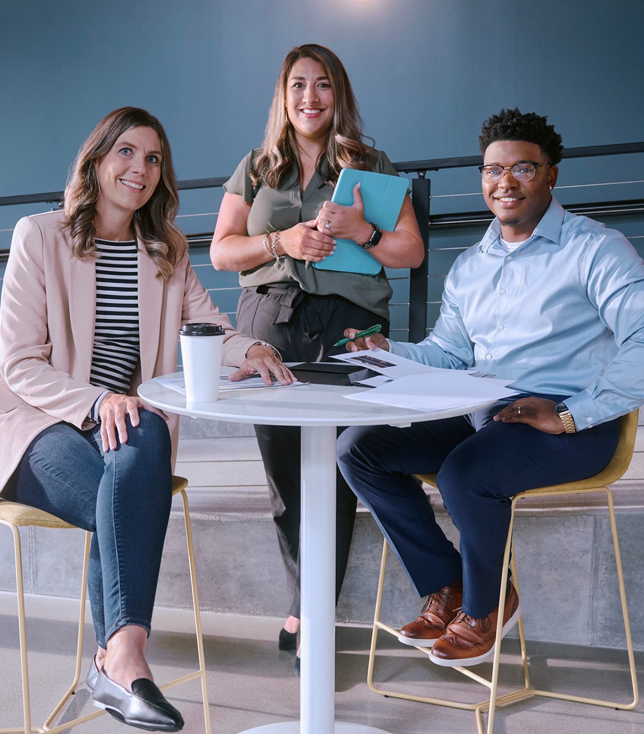 Two female employees and one male employee smiling and gathered around a tall white table.