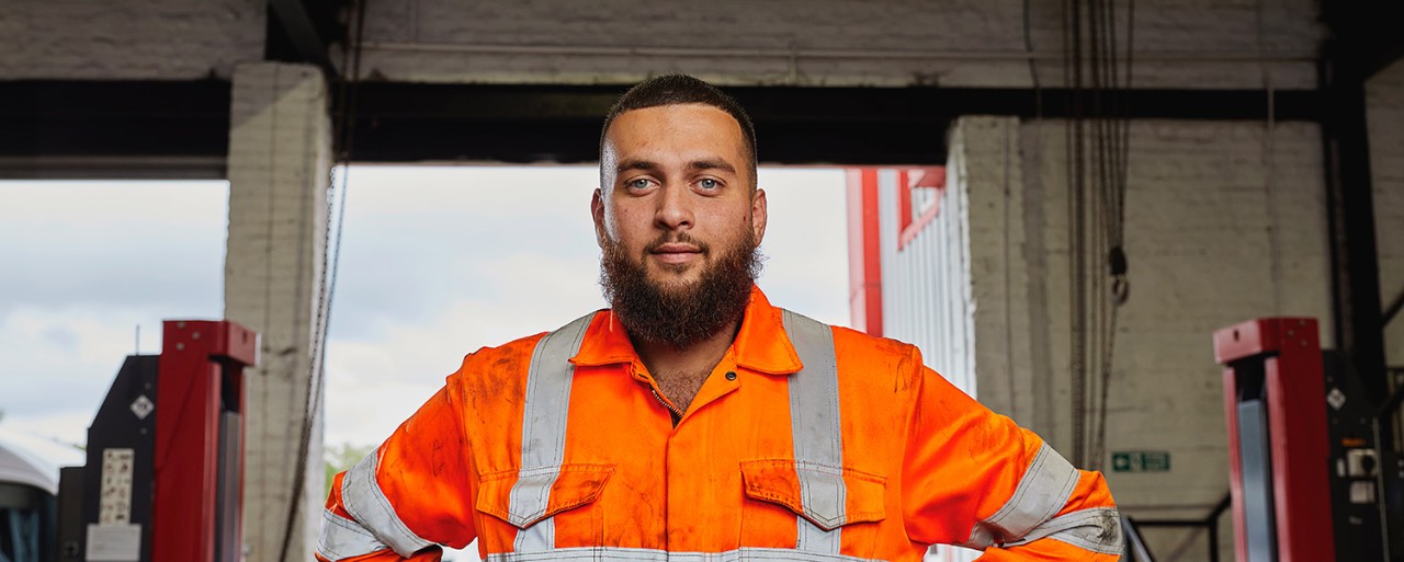 A male car mechanic with a beard in an orange jacket