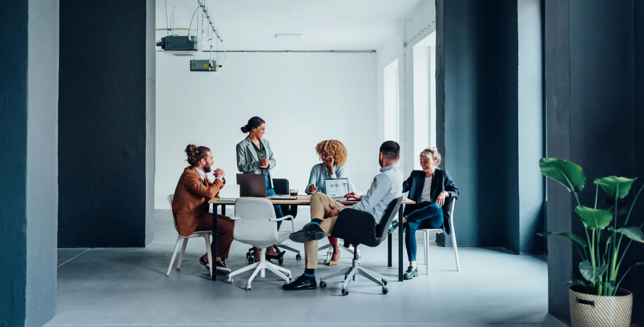 A woman addresses a group of colleagues seated around a conference table.