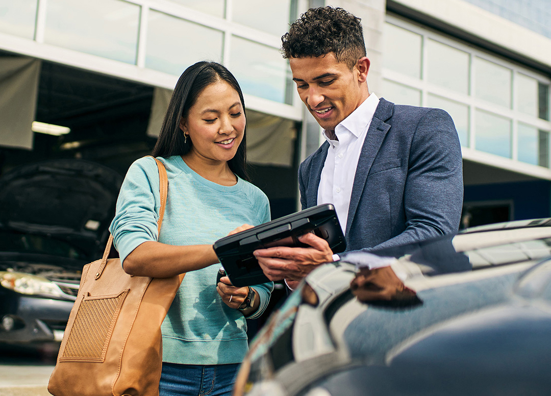 A man and woman look at an iPad together while standing next to a car