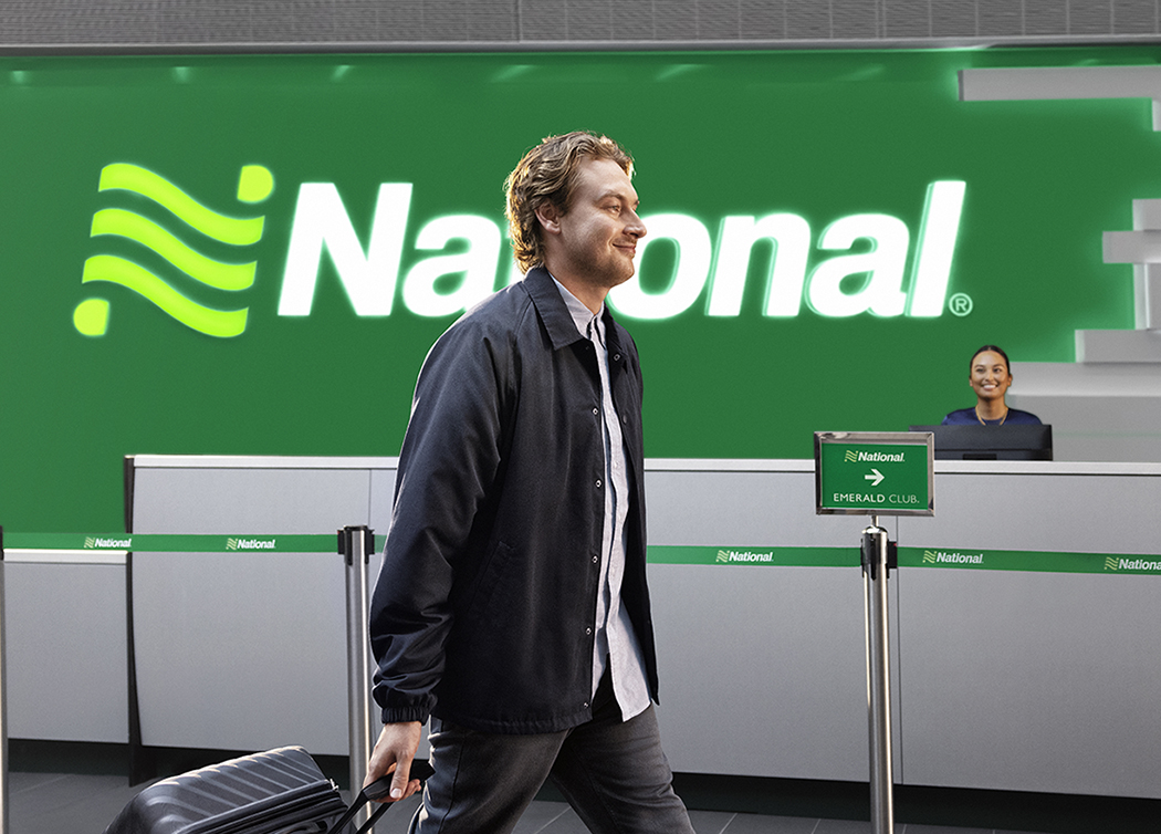 A male customer walks through an airport lobby as a female employee from the National Car Rental desk looks on