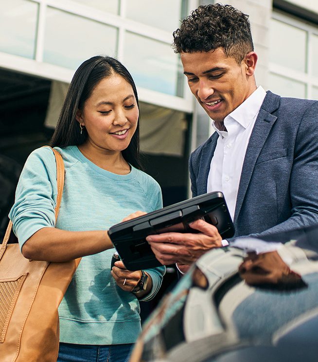 A man and a woman look carefully at an iPad outside of a vehicle