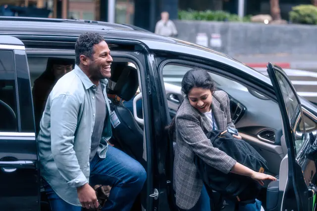 Two smiling men, one getting out of the passenger seat of a van, the other getting out of the middle row.