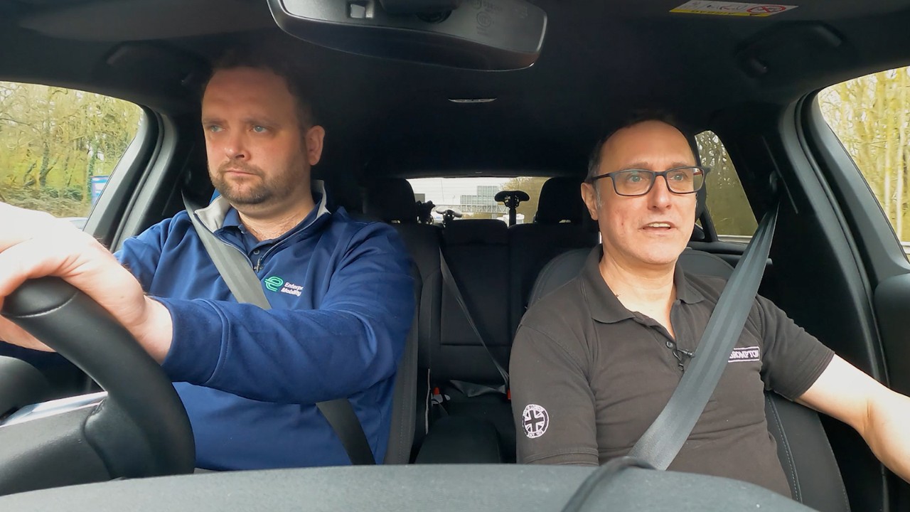 A white car drives on the road with green grass all around