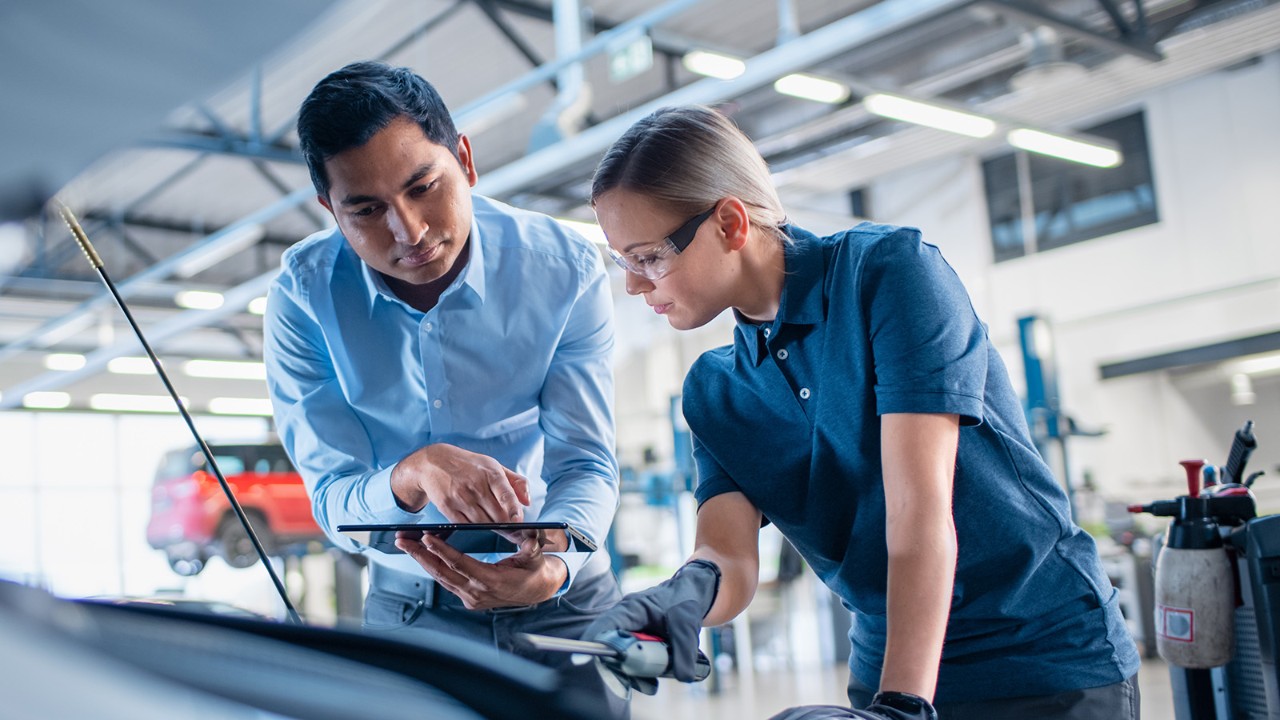 A man and woman in an auto body shop looking at an iPad
