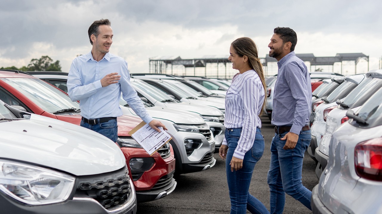 A Latin American salesman shows cars to a couple at a dealership