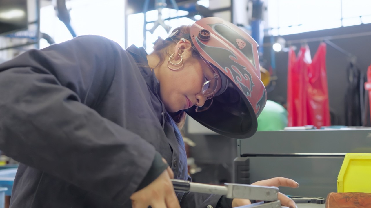 A female with a helmet, glasses and dark sweatshirt is focused on a task in the collision engineering space