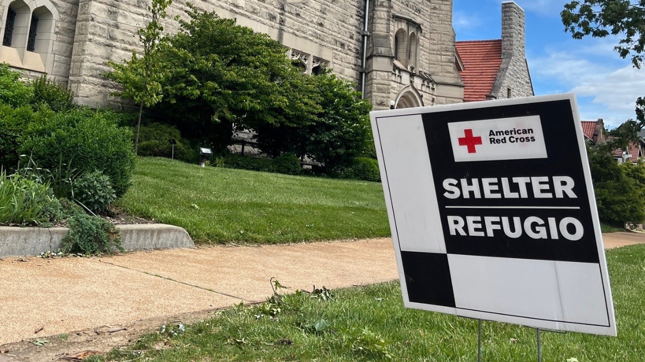 An American Red Cross shelter sign outside a building with green grass on a sunny day