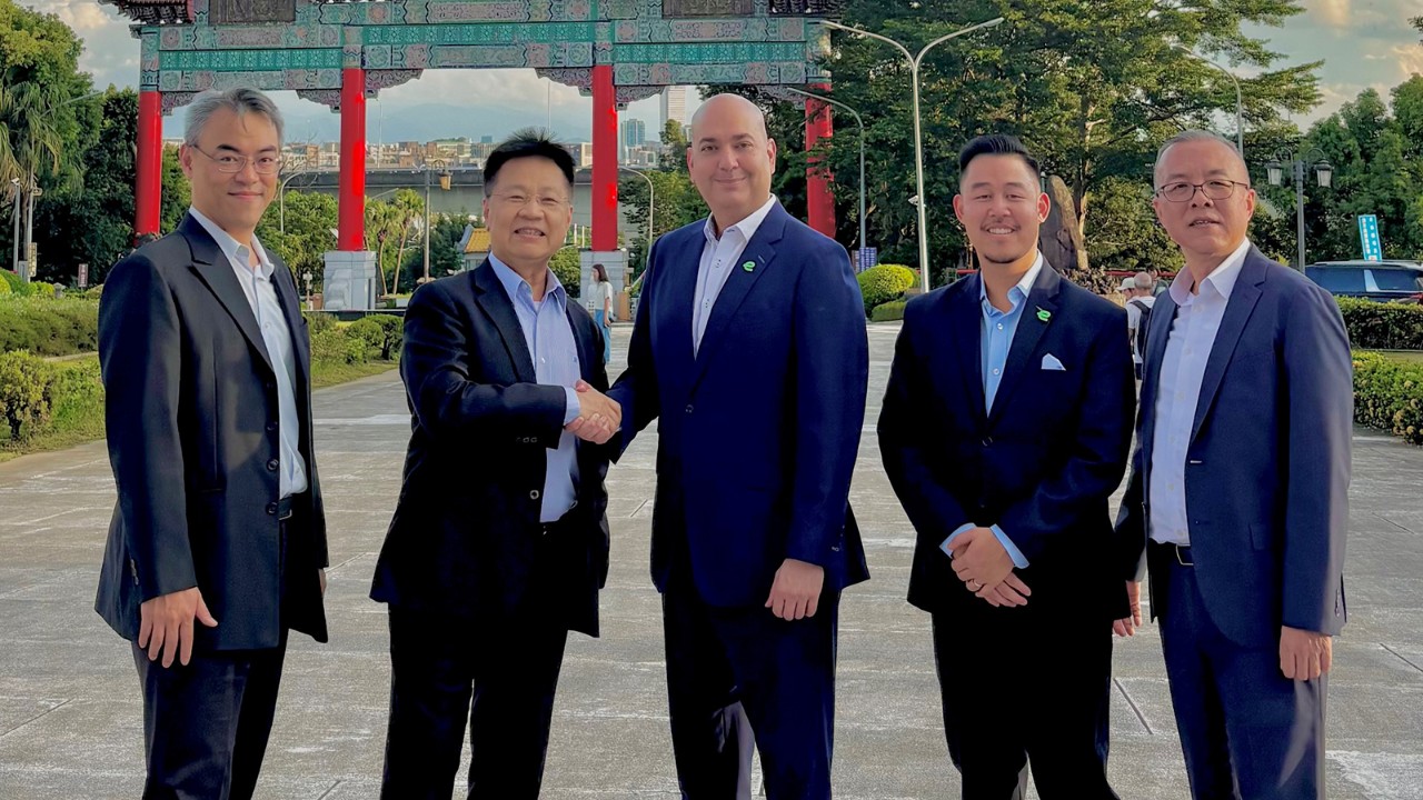Five men in dark suits smile for the camera while the two in the middle shake hands