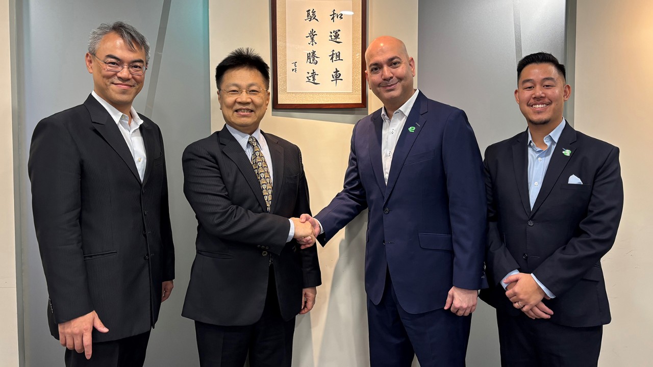 Four men in dark suits smile for the camera while the two in the middle shake hands