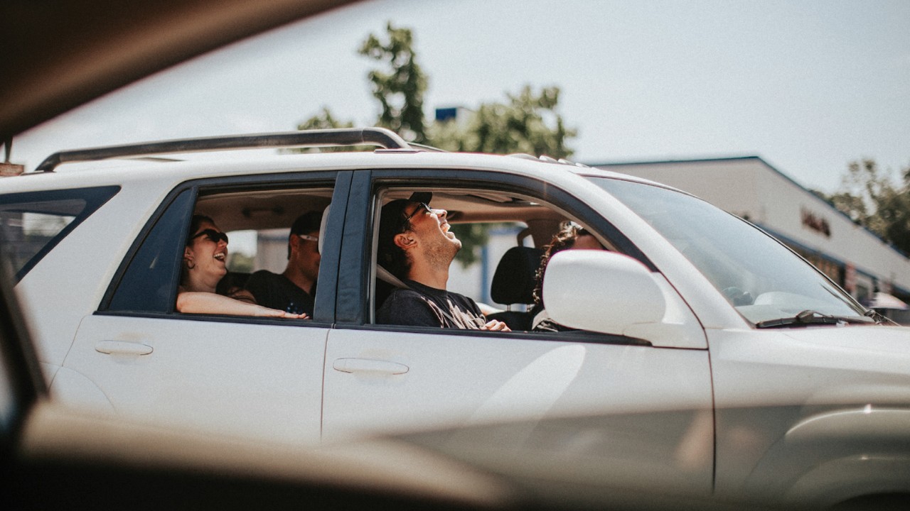 Four people laugh in a car with the windows down on a sunny day