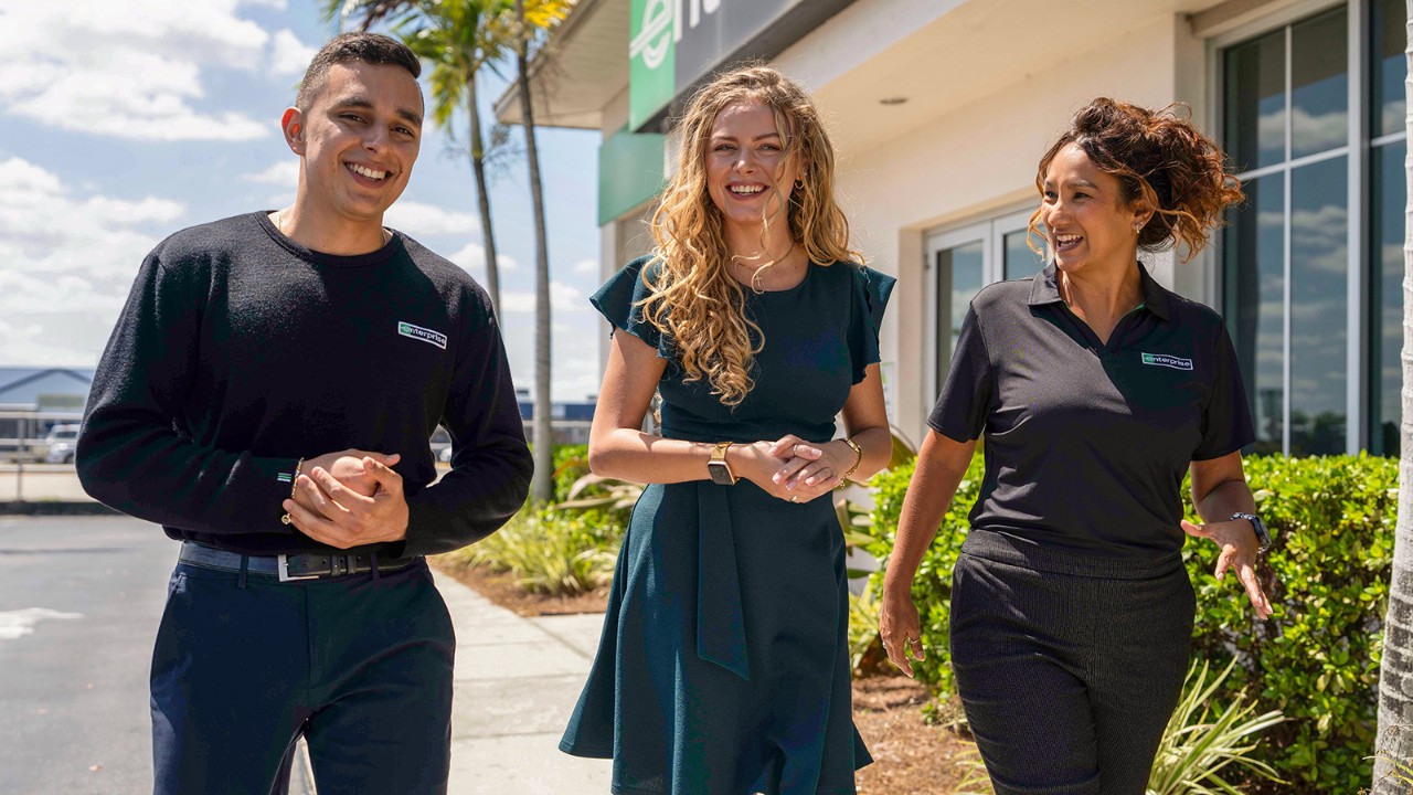 One male and two female employees walk and talk on a sunny day
