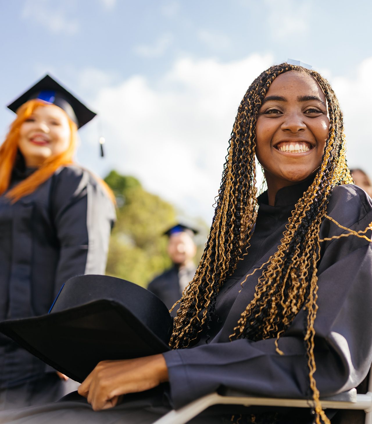 A female with long braided hair smiles at her college graduation ceremony