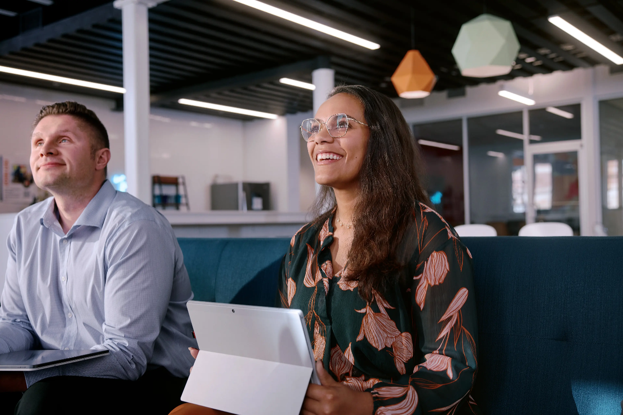 Una mujer sonriente sentada detrás de un mostrador con una computadora portátil abierta frente a ella.