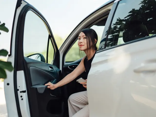 Mujer joven saliendo del asiento del conductor de una minivan blanca.
